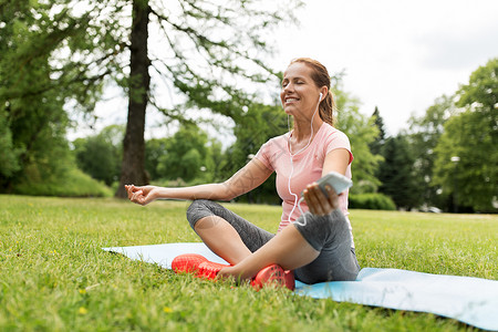 健身,运动技术妇女与智能手机耳机冥想瑜伽垫公园女人公园冥想瑜伽垫图片