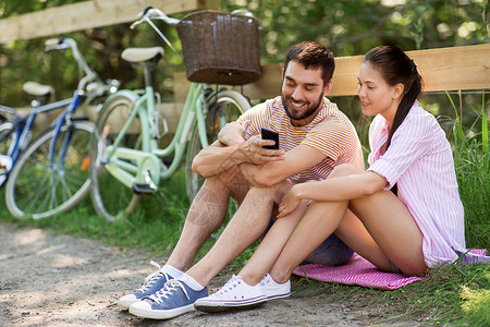 人,技术生活方式的快乐的夫妇与智能手机自行车夏季公园夏天公园里智能手机自行车背景图片
