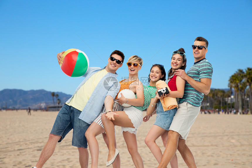 暑假,旅行假期群快乐的微笑朋友戴着太阳镜,带着沙滩球排球毛巾相机加州威尼斯海滩背景上威尼斯海滩上的快乐朋友图片