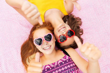 夏季时尚,休闲情人节微笑的十几岁女孩心形太阳镜上躺野餐毯上,竖大拇指戴太阳镜的十几岁女孩竖大拇指背景图片