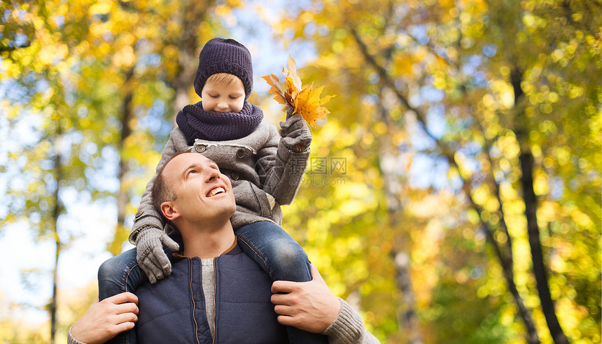 家庭,童父亲的快乐的父亲携带儿子与枫叶秋天的公园背景快乐的父亲带着秋天的枫叶带着儿子图片