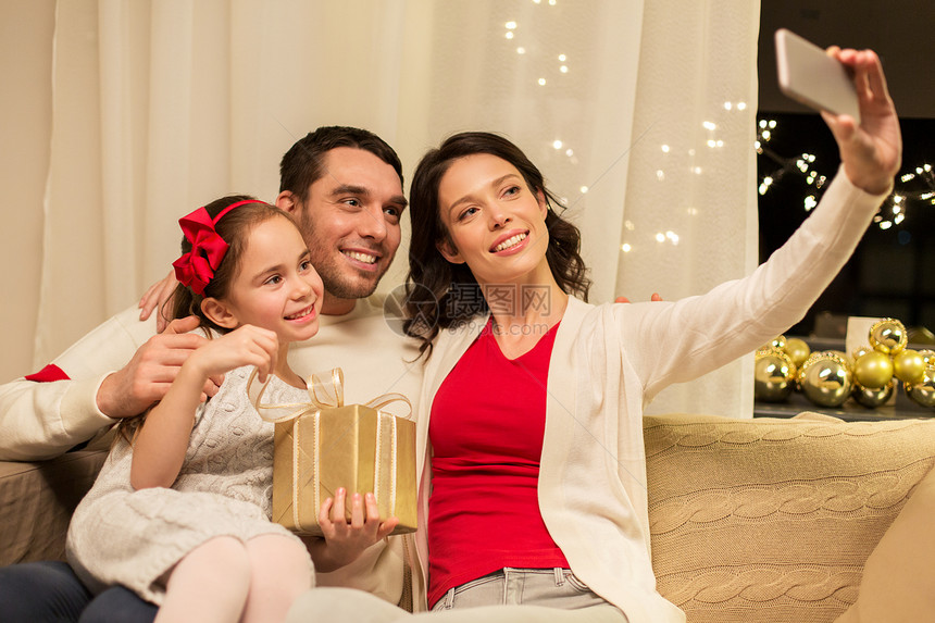 假期,家庭技术快乐的母亲,父亲小女儿带着诞礼物,家里用智能手机自拍家庭幸福,诞礼物家图片