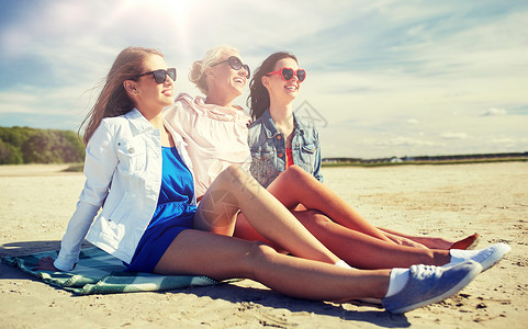 暑假,假期,旅行人们的群微笑的轻女,戴着太阳镜,穿着休闲服,沙滩毯子上晒太阳群戴太阳镜的微笑女人海滩上背景图片