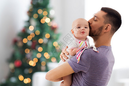 家庭,父爱假期快乐的父亲亲吻小婴儿女儿诞树灯的背景父亲诞树上亲吻小女儿图片