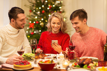 节日庆祝快乐的朋友与智能手机家里吃诞晚餐手机的朋友家庆祝诞节图片