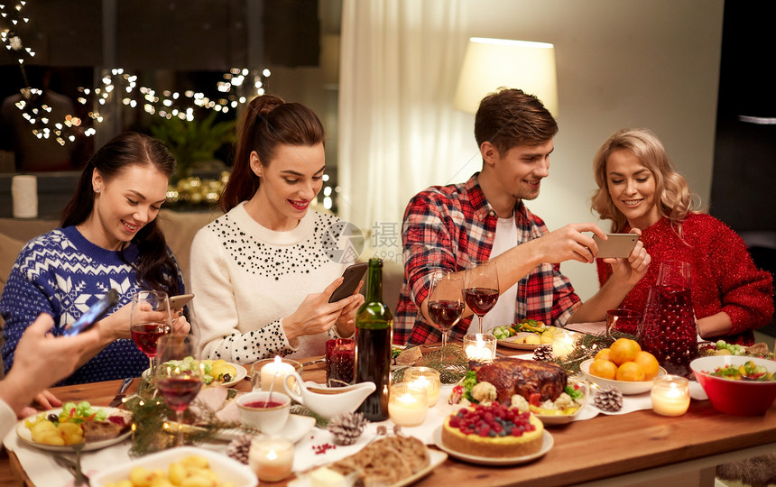 节日庆祝快乐的朋友与智能手机家里吃诞晚餐智能手机的朋友吃诞晚餐图片