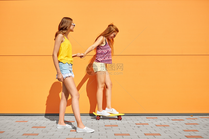 友谊,休闲人的快乐的十几岁女孩朋友骑滑板牵手城市街道夏天十几岁的女孩城市街道上骑滑板图片