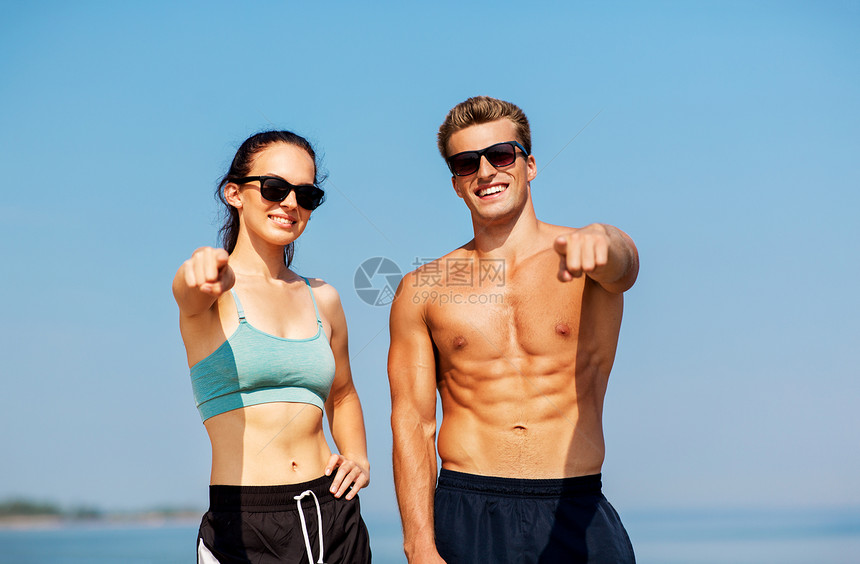 健身,运动生活方式的快乐的夫妇穿着运动服装太阳镜海滩上指着你海滩上穿着运动服装墨镜的幸福夫妇图片