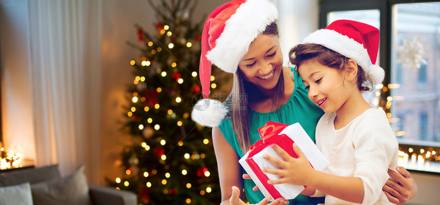 节日家庭快乐的母亲女儿戴着诞帽,房间里礼品盒,带诞树背景快乐的母亲女儿带着诞礼物图片