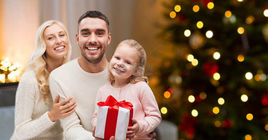 家庭,假期人的快乐的母亲,父亲小女儿,带着礼品盒坐家里的沙发上,背景诞树灯幸福的家庭家里带着诞礼物图片