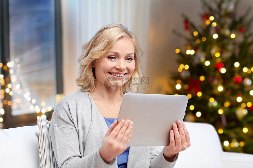 技术,假日人的快乐的中妇女与平板电脑家里的诞树灯光背景诞节家用平板电脑的快乐女人图片