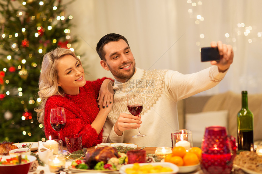 诞节,假日,技术人的快乐的夫妇家里吃晚饭时用智能手机自拍快乐的夫妇诞晚餐上自拍图片