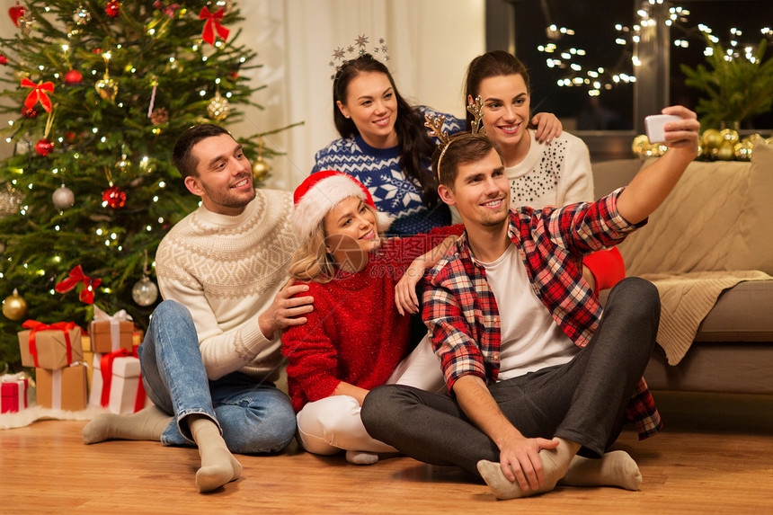 庆祝假期快乐的朋友戴着眼镜,家里的聚会上庆祝诞节,用智能手机自拍朋友们庆祝诞节自拍图片