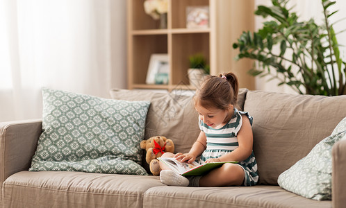 童人的小女孩坐沙发上看书,玩具泰迪熊家小女孩家看书图片