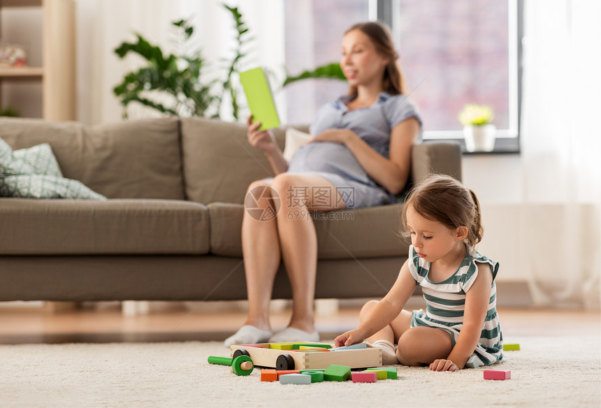 童人的快乐的三岁女婴玩玩具积木怀孕的母亲家看书快乐的女婴家里玩玩具积木图片