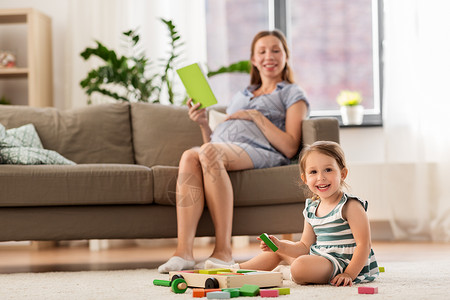 童人的快乐的三岁女婴玩玩具积木怀孕的母亲家看书快乐的女婴家里玩玩具积木背景图片