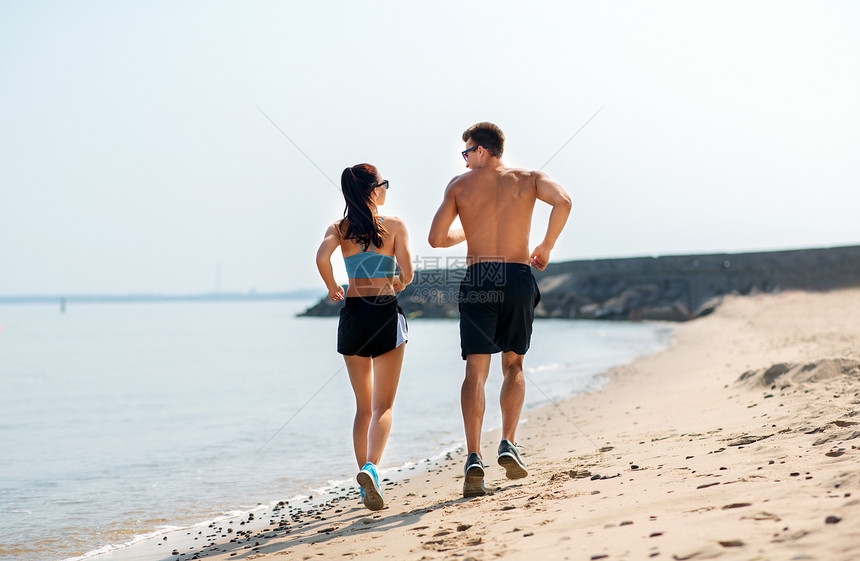 健身,运动生活方式的快乐的夫妇沿着夏天的海滩跑步穿着运动服的夫妇海滩上跑步图片