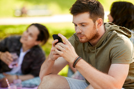休闲,技术人的女人用智能手机野餐与朋友夏季公园男人朋友野餐时用智能手机图片