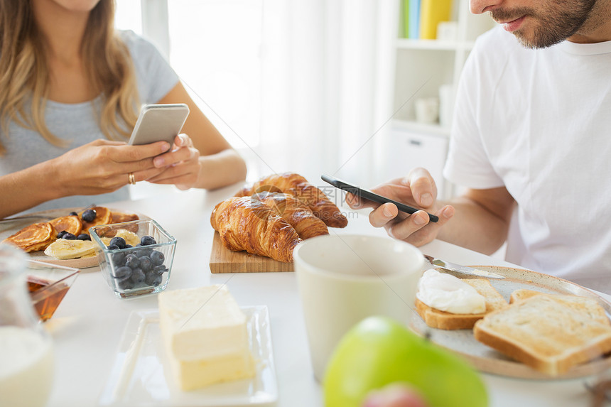 食物技术亲密的夫妇与智能手机家里吃早餐早餐时用智能手机夫妇图片