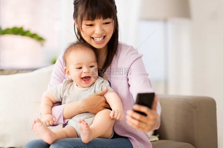 家庭母亲的快乐微笑的轻亚洲母亲与小婴儿儿子家里用智能手机自拍亚洲母亲带着小儿子家自拍图片