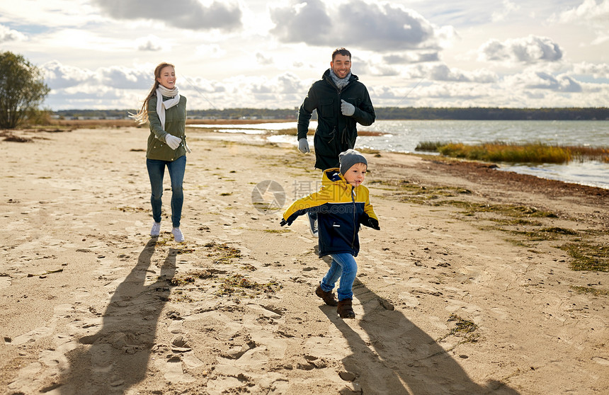家庭,休闲人的快乐的母亲,父亲小儿子沿着秋天的海滩跑步幸福的家庭沿着秋天的海滩奔跑图片