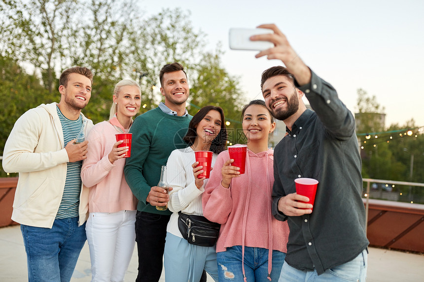休闲人们的快乐的朋友与饮料采取自拍智能手机屋顶聚会夏天饮料的朋友屋顶派上自拍图片