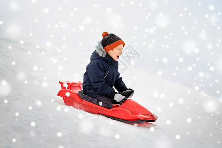 骑着摩托男孩童,雪橇季节的快乐的小男孩滑雪橇下雪山冬天的户外快乐的男孩冬天乘雪橇滑下雪山背景