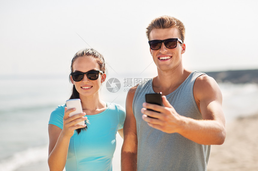 健身,运动生活方式的快乐的夫妇穿着运动服装太阳镜,海滩上智能手机穿着运动服智能手机的夫妇海滩上图片
