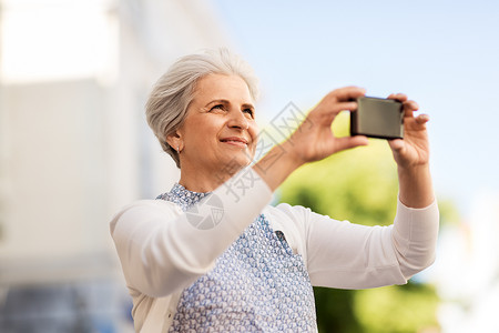 旅游,旅游技术快乐的老年女子拍摄智能手机城市老妇女城市用智能手机拍照图片