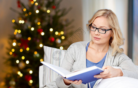 假期,休闲视觉中妇女戴着眼镜家里阅读诞树背景的书诞节戴眼镜看书的女人图片