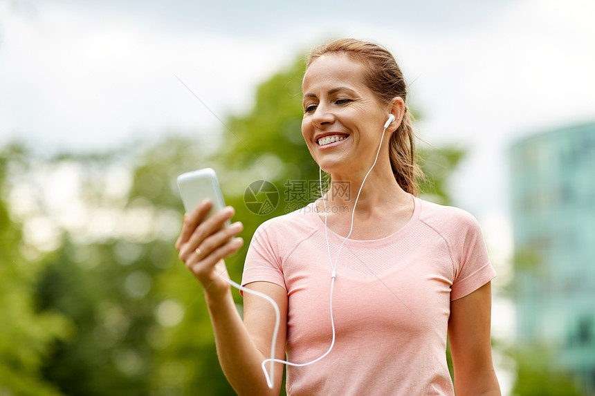 健身,运动健康的生活方式微笑的女人城市公园智能手机上听音乐夏天公园的智能手机上听音乐的女人图片