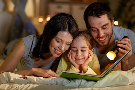 人们家庭的快乐的母亲,父亲小女儿家里晚上床上用手电筒看书快乐的家庭阅读书晚上床上家背景图片