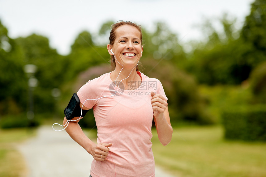 健身,运动健康的生活方式微笑的女人戴着智能手机,夏季公园慢跑听音乐带耳机的女人公园里增加慢跑图片