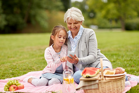 家庭,休闲技术快乐的祖母孙女与智能手机夏季公园野餐祖母孙女公园牢房图片