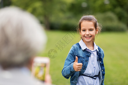 家庭,休闲技术的快乐的小女孩被拍照拇指夏季公园女孩被拍照并竖大拇指背景图片