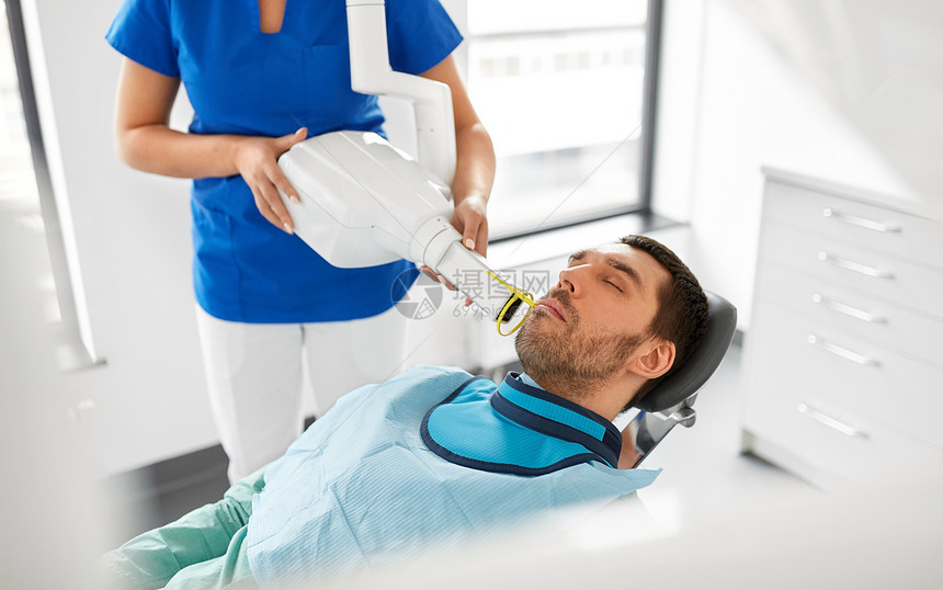 医学,牙科保健女牙医用X光机扫描男病人牙齿牙科诊所牙科医生病人的牙齿进行牙科X光检查图片