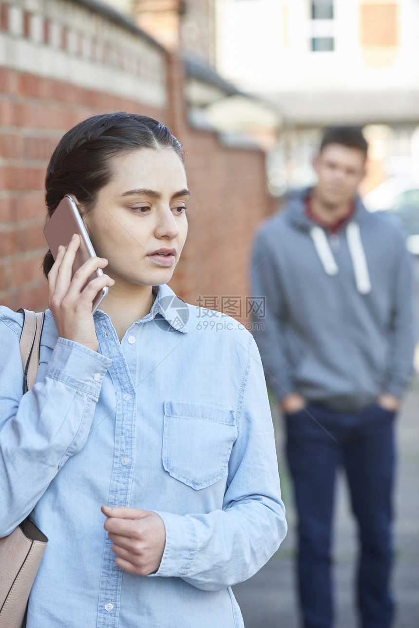 轻的女人城市街道上被跟踪时,用手机呼救图片