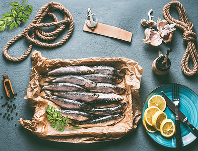 厨房桌子背景上的生沙丁鱼配料柠檬,大蒜草药,用于美味的海鲜烹饪鱼类的烹饪准备背景图片