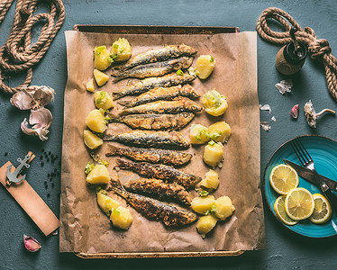 烤沙丁鱼土豆烤盘上,配料柠檬,大蒜草药,供美味的海鲜食用鱼类的烹饪准备图片