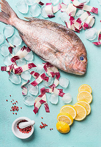 原始整条鱼浅绿色背景下,冰块配料,顶部视图海鲜粉红色多拉多烹饪准备图片