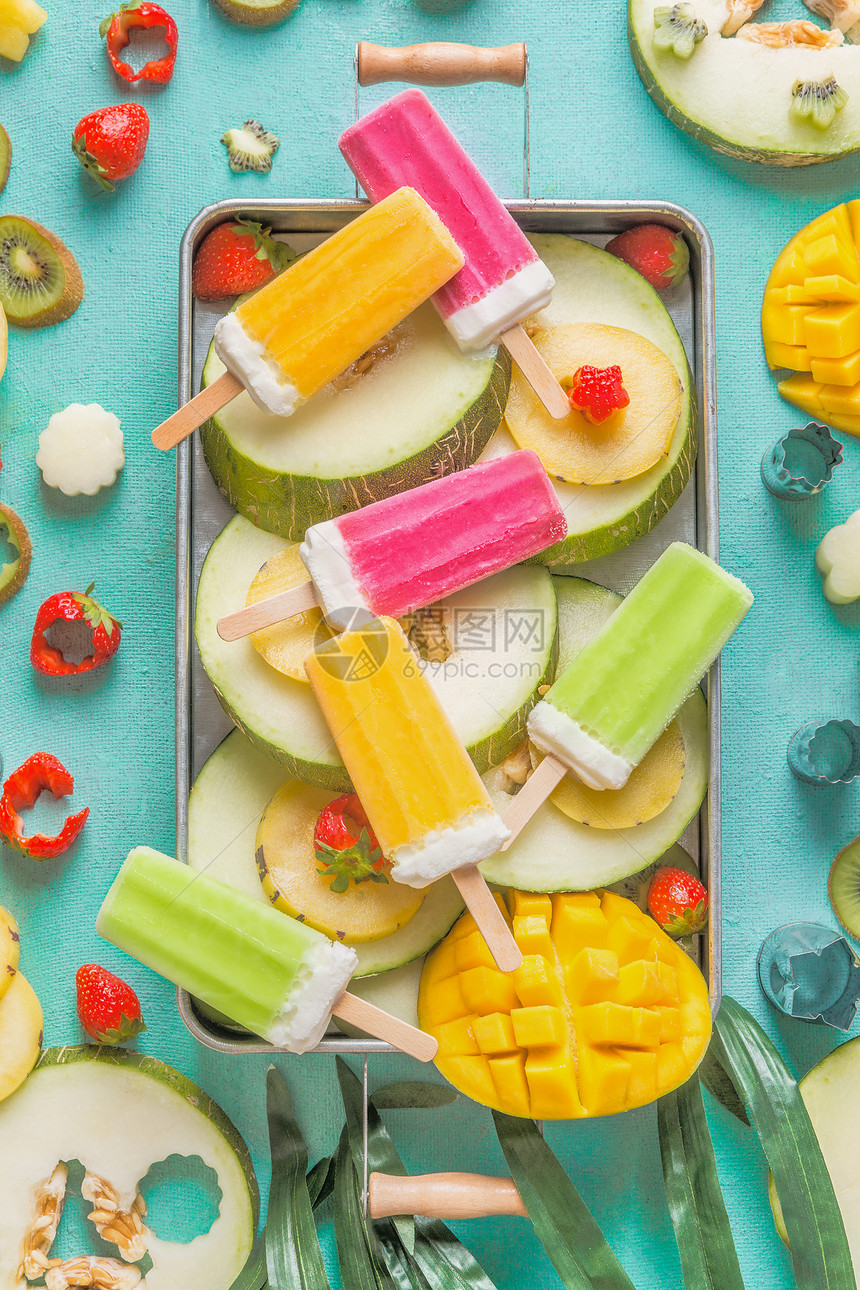 托盘与彩色冰淇淋冰棒与新鲜切片水果浆果成分浅蓝色背景,顶部视图,平躺冷冻热带果汁自制冰淇淋派图片