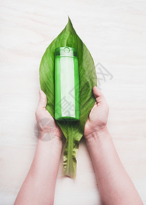 女手大绿叶与化妆品瓶产品白色背景,顶部视图纯素天然护肤美容理念图片