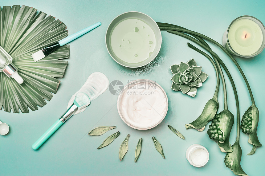天然化妆品工具,用于家庭部皮肤护理与鲜花绿色热带树叶,顶部视图,平躺蓝绿色背景上的血清罩蜡烛美丽的图片