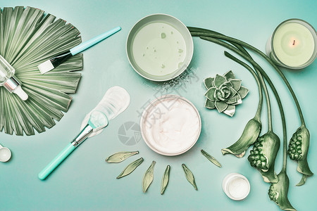 天然化妆品工具,用于家庭部皮肤护理与鲜花绿色热带树叶,顶部视图,平躺蓝绿色背景上的血清罩蜡烛美丽的背景图片