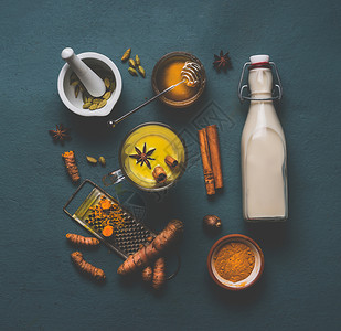 杯健康的金色姜黄香料牛奶,配料豆蔻,姜黄,肉桂,蜂蜜生姜灰色背景,顶部的视图免疫促进补救,排节食的背景图片