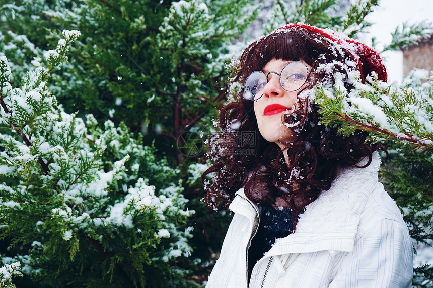 轻漂亮的女人享受着被树木包围的雪冬图片