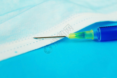 带蓝色背景的医用罩上针头的注射器的详细图片