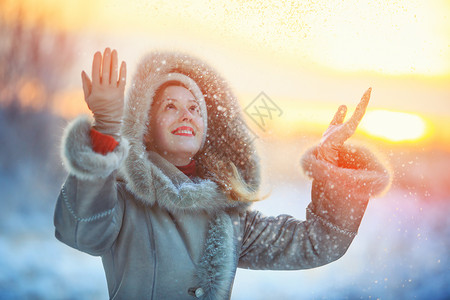 轻快乐的女人穿着温暖的冬装,吐雪红色的日落颜色图片