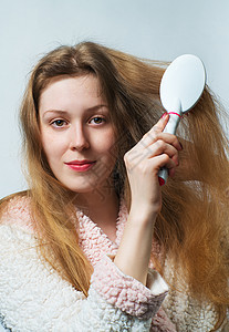 轻的金发女人穿着浴袍梳头后洗白色背景上图片