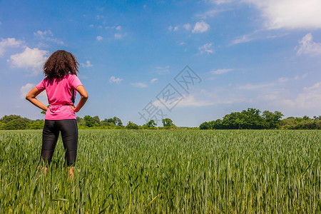 后视镜的轻女女孩,女跑步者,手臀部站绿色的田野与蓝天图片